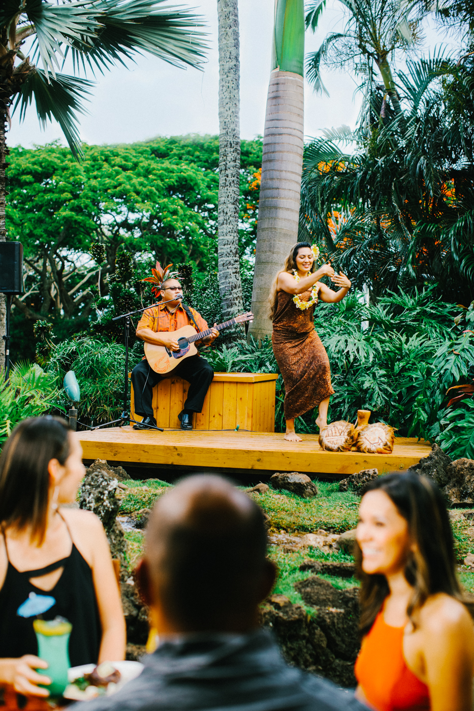 Group of people enjoying meal with live music and hula dancers in the background